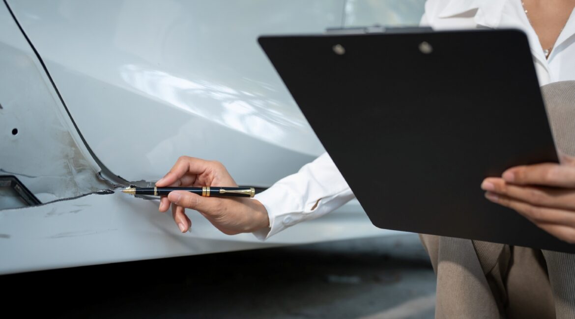 female insurance adjuster inspecting lower front driver side door collision damage with clipboard in hand